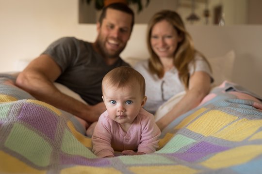 Parents With Baby Lying On Bed In Bedroom