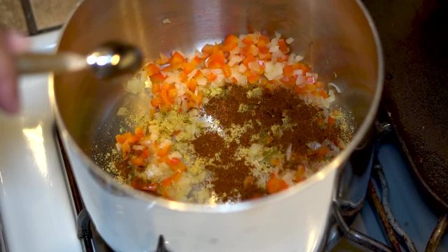 Sprinkling spices on top a sauteed sauce base in a pot