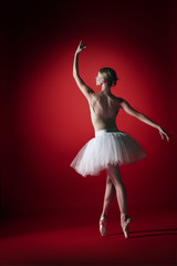 Fototapeta na wymiar Young graceful female ballet dancer or classic ballerina dancing at red studio. Caucasian model on pointe shoes