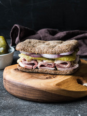 Homemade sandwich with boiled pork, pickled cucumbers, onions and mustard on the board