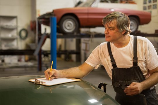Male mechanic writing on clipboard