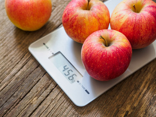 Red apples on kitchen scale on wooden background. Product weighing