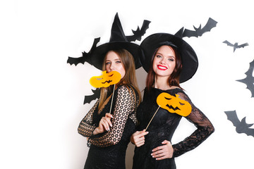 Two happy women in black witch halloween costumes with pumpkin on party over white background