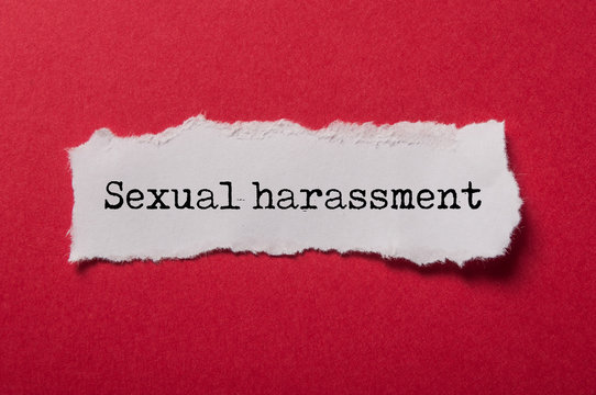 closeup of white torn paper on red paper background with text - Sexual harassment