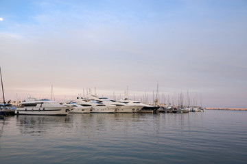 Beautiful port of Alicante, Spain at Mediterranean sea. Luxury yachts, ships, ferries and fishing boats sailing and standing in rows in harbor. Rich people traveling around the world. Sunset evening