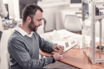 Fototapeta premium Useful information. Smart bearded man reading how to use 3D printer trying to make a layout