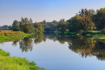 Calm surface of the river against blue sky at summer morning. River landscape at sunrise