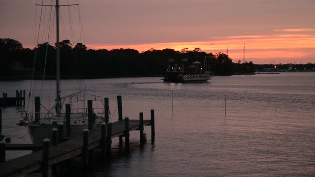 Beautiful sunset looking out passed a dock and parked sailboat as an old fashion paddle boat passes.
