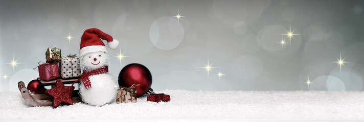 Snowman with Christmas gifts on the sledge isolated on gray winter background.