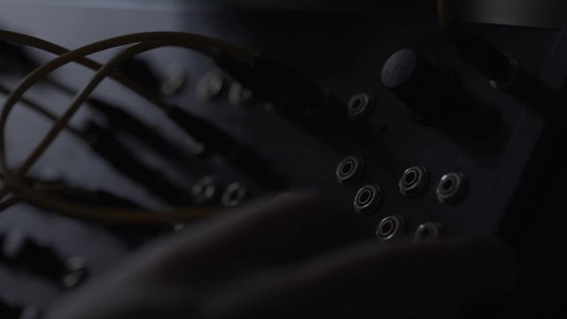 Music producer pluging in audio cables on analog synthesiser and turning it on