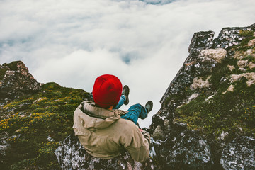 Man relaxing sitting alone on cliff edge rocky mountains above clouds travel adventure lifestyle...