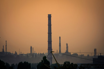 Industrial landscape at the sunset. Tall pipes and chimneys in fog at orange sky at the background