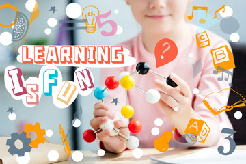 cropped shot of smiling schoolchild holding molecular model, with icons and lettering "learning is fun"