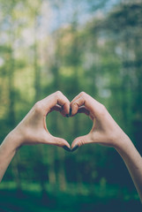 Girl demonstrating a heart shape gesture against spring forest covered with sunlight. Vintage retro...