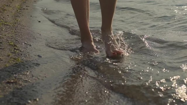 Female legs in sea waves. Close up of woman legs walk on water, slow motion 