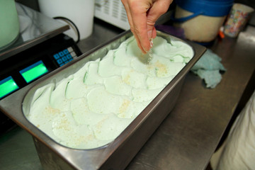 Confectioner in chef uniform is working at ice cream factory. Woman is decorations of italian creamy mint ice cream flavors in steel container. Manufacture, industry, production, people concept.