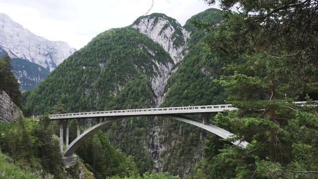 Arched bridge over a mountain river gorge in European Alps with mountain in background and cloudy skies. Mangart saddle pass in Julian alps, Slovenia