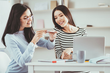 New technology. Nice young woman taking a photo while studying together with her friend