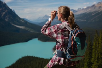 Female hiker looking through binoculars at countryside