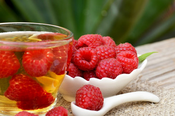 Raspberry tea with fresh picked berries in a glass transparent cup on old wooden table in the garden.Natural herbal beverage.Selective focus.