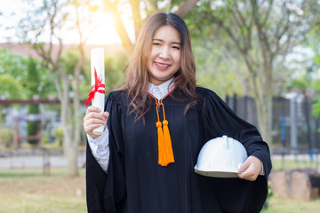 Beautiful Attractive Asian woman graduate in gown smile with engineer white helmet feeling so proud...