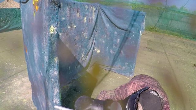 POV shot of paintballer playing in outdoor arena getting hit by paintballs, also hitting camera.