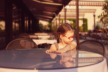 young girl with glasses and dress is sitting at a table in a cafe