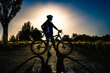 Fototapeta na wymiar Silhouette of a girl with a bicycle at sunset in the summer