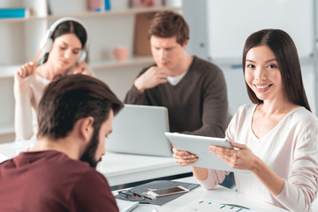 Modern students. Positive Asian student smiling while using a tablet