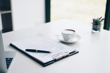 Pen on contract sheet and business document ,near coffee cup and laptop computer in home office, Business and Office concept.