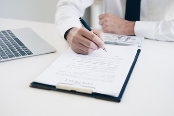 Businessmen holding pen to write business document and contract sheet while sitting at desk with coffee cup, laptop computer and money in home office, Business and Office concept.