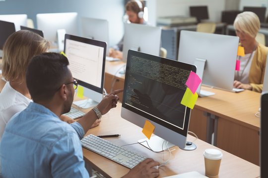 Executives discussing over desktop pc at desk