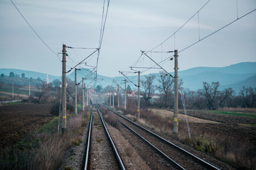 Fototapeta na wymiar Eastern European railroad across Transilvania. Mountain landscape in the background. Scary, dangerous scene in winter with naked trees and polluted nature