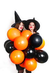 Two happy sexy women in black witch halloween costumes with orange and black balloon on party over white background