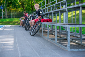 Cyclists resting and sitting on metal bench next to outdoor basketball court and watching the game.  Healthy lifestyle and outdoor activities in  summer, spring and autumn
