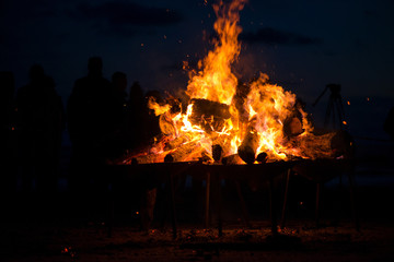 Large burning bonfire with soft glowing flame and sparkles flying all around. Romantic summer evening, people relaxing and enjoying calmness at the seaside during the Night of ancient lights