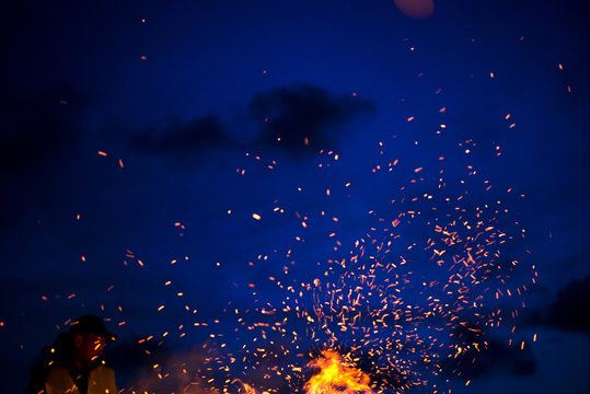 Large burning bonfire with soft glowing flame throws flying sparkles all around. Romantic summer evening, people relaxing and enjoying calmness at the seaside during the Night of ancient lights