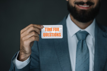 cropped view of businessman smiling and showing business card with world map and "time for questions" lettering