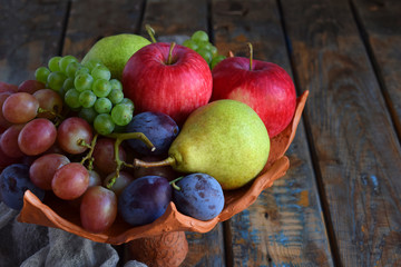 Autumn still life for thanksgiving with autumn fruits and berries on wooden background - grapes, apples, plums, viburnum, dogwood. Raw food. Copy space