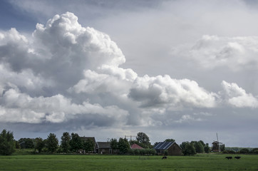 Dramatic cloudscape over a polder landscape with grassland, a farm and a windmill near Nigtevecht, The Netherlands