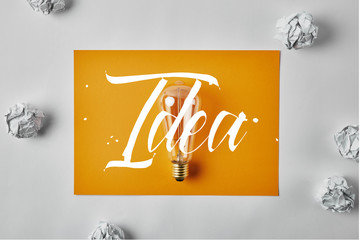 Idea concept with top view of incandescent lamp on blank yellow paper surrounded with crumpled papers