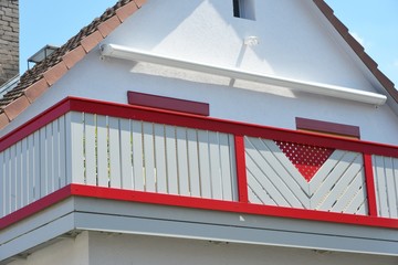 Balkon mit rot-weißem Holzgelander und Windmessgerätund elektrischer Markise an einem Wohnhaus