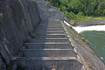 Dam wall and overflow of Iskar Dam. Water flowing over a dam wall. Mist rising above the Iskar dam wall. Cascade from a hydroelectric plant. Lake water release. Water plums on hydropower station.