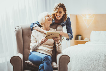 Happy females. Amazing female person sitting on cozy armchair and holding photo frame