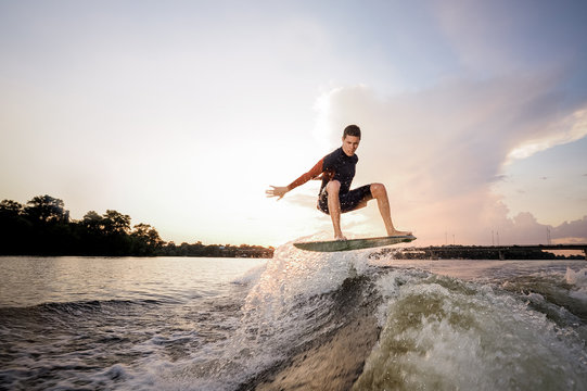 Young attractive man riding on the wakeboard on the background of lakeside and bridge