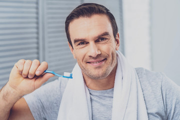 Brushing teeth. Pleasant-looking mature man smiling broadly while brushing his teeth early in the morning