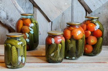 Glass jars with canned tomatoes and cucumbers. Wooden background