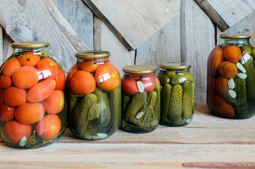 Row of glass jars with canned tomatoes and cucumbers. Wooden background