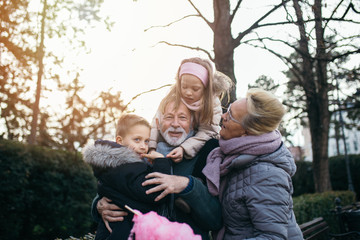 Grandparents having fun with their grandchildren in city park. - obrazy, fototapety, plakaty
