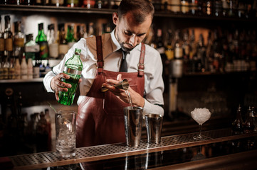Bartender pourring an achoholic drink from the measuring cup into the steel shaker